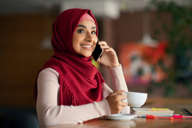 istock Happy religious middle-eastern lady having phone conversation, cafe interior 1352726526