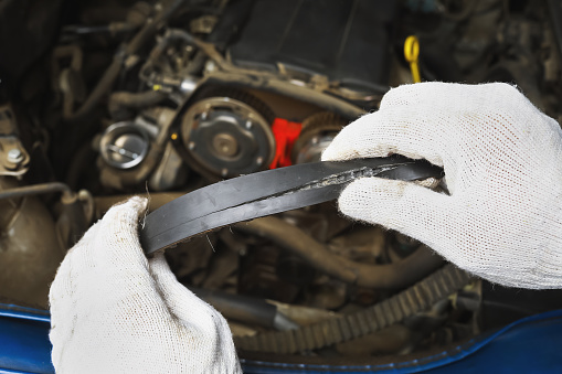 An auto mechanic shows a timing belt burst from the back side, close-up