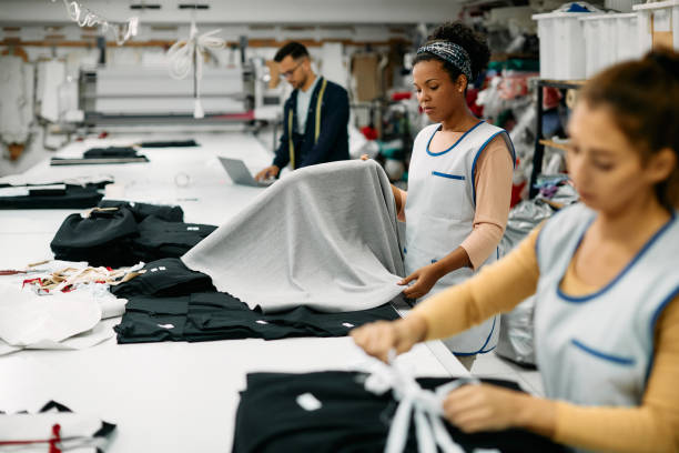 impiegato della fabbrica tessile afroamericana che lavora con il tessuto alla linea di produzione. - sewing women tailor textile foto e immagini stock