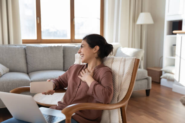 istock Indian woman sit on armchair with computer holds cellphone laughing 1352734429
