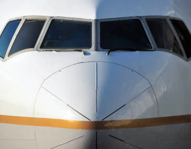 Front view of an airliner nose cone and cockpit windows (Boeing 777-200), no markings - starboard is sunny, portside in the shade.