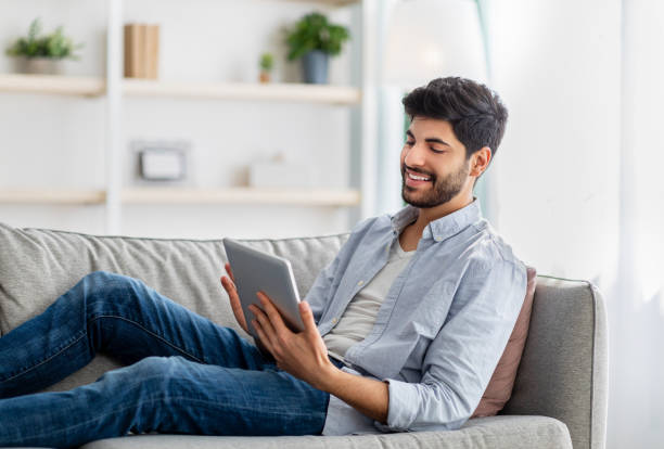 istock Relaxed arab guy resting on sofa with digital tablet, browsing social networks or shopping online, free space 1352737378