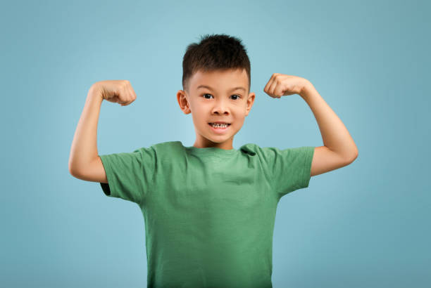 istock Funny Little Asian Boy Showing Biceps And Looking At Camera 1352737449