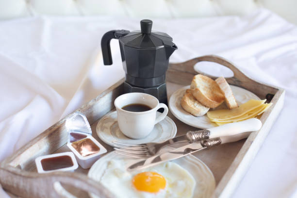 istock A breakfast tray with a fried egg, a cup of black coffee and a coffee pot is on a white bed. Retro style. Free space for text. 1352738283