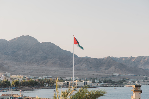 A Celebration of National Pride. Man holds waving national flag of United Kingdom standing at the top at sunset. Beautiful mountains and sea on background.