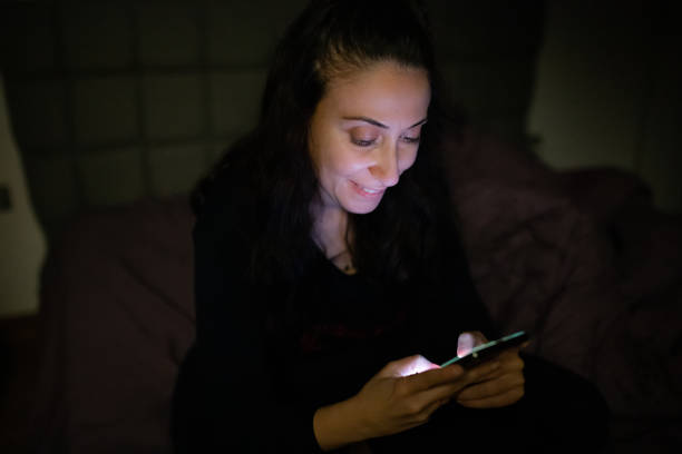 istock Young woman using mobile phone in dark room at night 1352745203