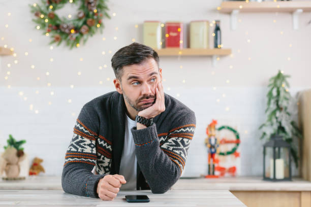 수염을 가진 남자는 지루하고 우울증에 전화를보고, 크리스마스에 집에서 혼자 - christmas present men male people 뉴스 사진 이미지