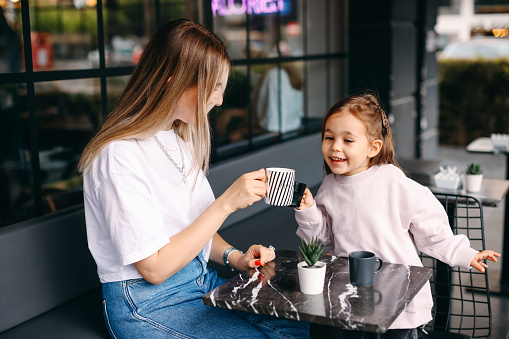 Young kid girl smiling. She sitting in cozy cafe with light interior and spending time with happy mum