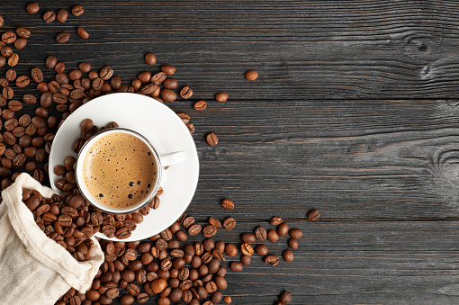 A cup of coffee and coffee beans on a wooden background. Top view. Free space for text. High quality photo