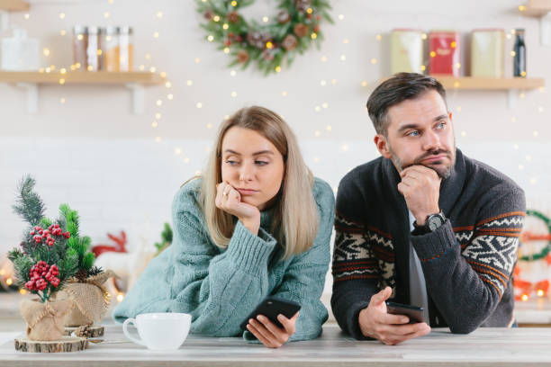 Young family couple quarreled over mobile phone and social networks, man and woman sad during the New Year holidays and Christmas Young family couple quarreled over mobile phone and social networks, man and woman sad during the New Year holidays and Christmas arguing couple divorce family stock pictures, royalty-free photos & images