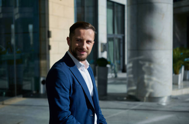 istock Confident attractive handsome successful businessman developer entrepreneur in business suit smiling looking aside standing outdoor on a modern corporate high-rise building glass entrance background 1352748796