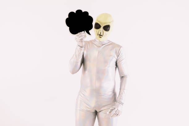 istock Person dressed in silver suit and green alien mask, holding a comic speech bubble with hand, on white background 1352751798