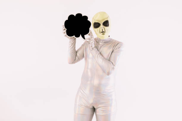 istock Person dressed in silver suit and green alien mask, holding a comic speech bubble with hand, on white background 1352751804
