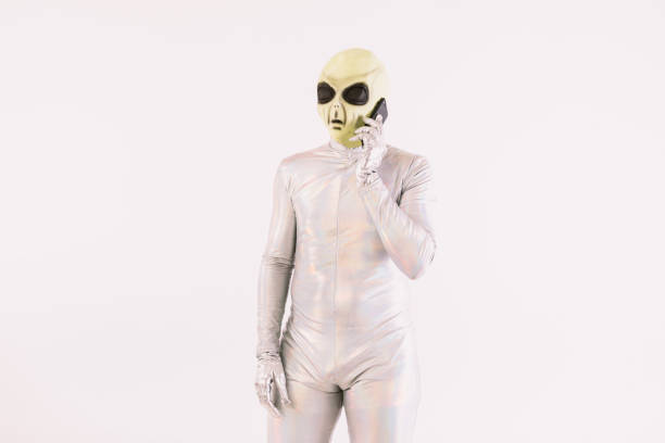 Person dressed in silver suit and green alien mask talking on the mobile phone over white background stock photo