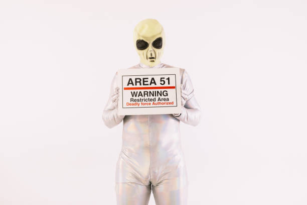 Person dressed in silver suit and green alien mask, holding an Area 51 poster, on white background stock photo