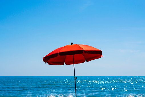 A lonely bright red beach umbrella in the center of the picture on a sunny summer day with blue see and the sky in the background. Summer concept.