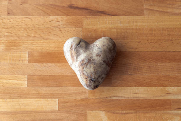 素晴らしいバレンタインデーやロマンチックな背景画像を作る木製のまな板の上に生の未調理のハート型の白いジャガイモのクローズアップ写真。 - heart shape raw potato food individuality ストックフォトと画像