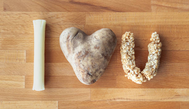 私はあなたが木のまな板の上にuの形をしたモッツァレラの弦のチーズスティック、ハート型のジャガイモとグラノーラバーを含む食品を使用して綴られたメッセージを愛しています。 - heart shape raw potato food individuality ストックフォトと画像