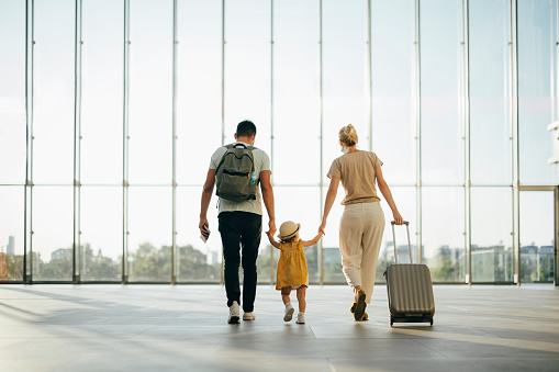 Back view of husband and his wife walking with their little girl and suitcase at the airport