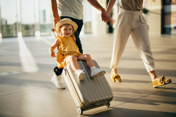 Unrecognizable parents walking with their cute little girl sitting on luggage at the airport