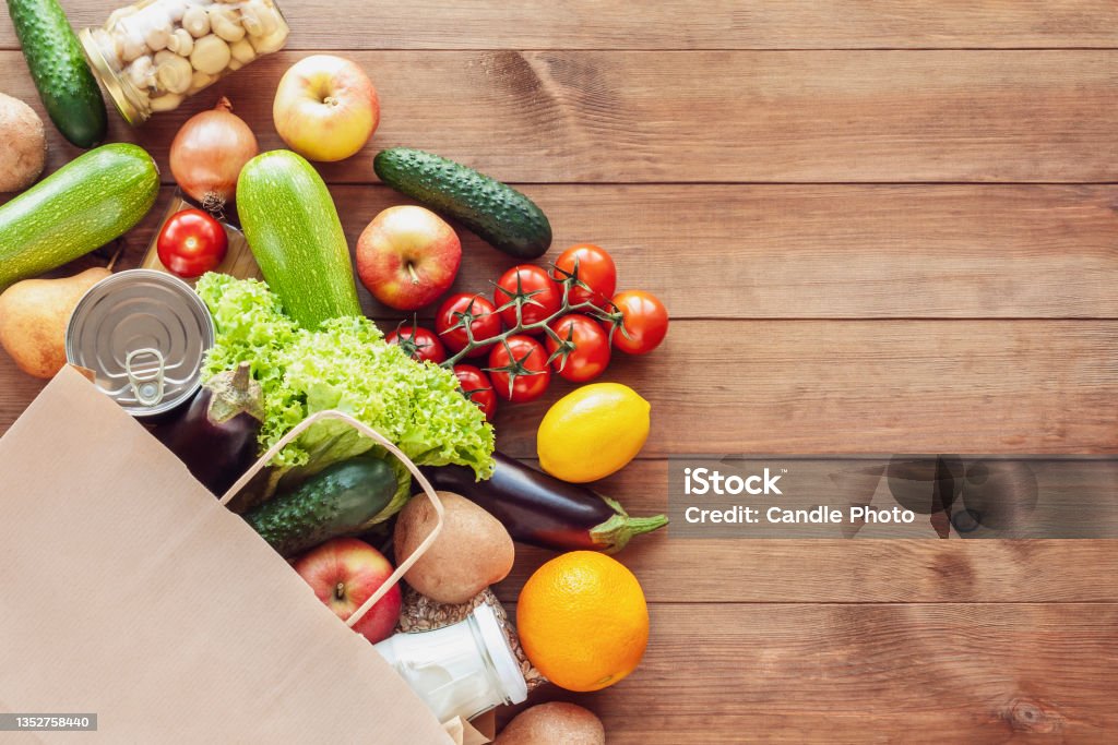 Paper shopping food bag with grocery and vegetables Paper grocery bag with fresh vegetables, fruits, milk and canned goods on wooden backdrop. Food delivery, shopping, donation concept. Healthy food background. Flat lay, copy space. Supermarket Stock Photo