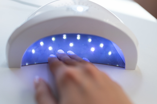 Mano femenina dentro de la máquina de secado de luz UV en el salón de uñas photo