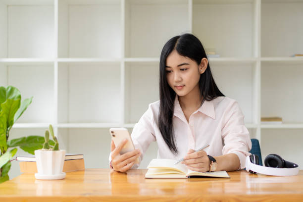 istock Young Asian students are smiling and looking at the camera in studying the future for themselves or personal learning ideas. Smiling young student studying online at home with books and laptop. 1352774768