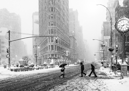 New York City, New York, USA - February 13, 2014: Pedestrians walking  on Snow-Covered Streets of Midtown Manhattan. Flatiron Building seen on the background at 175 Fifth Avenue, New York