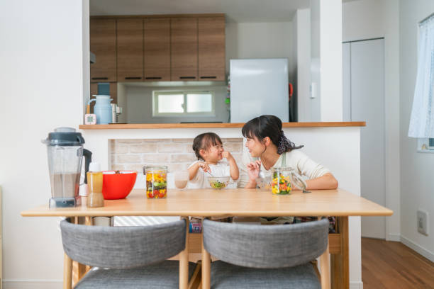 mother and her small daughter enjoying eating salad and drinking smoothie at home - salad japanese culture japan asian culture imagens e fotografias de stock