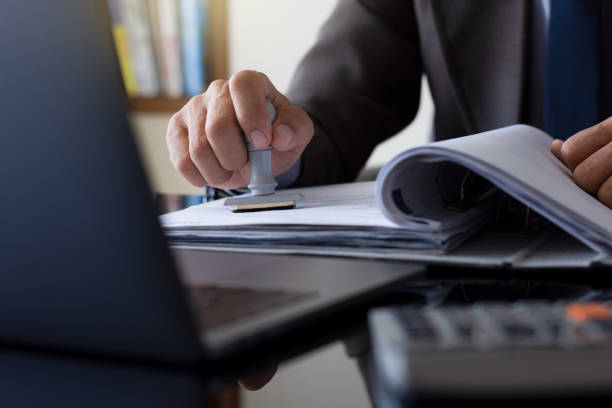 Businessman in suit hand stamping rubber stamp on document in file folder Businessman in suit hand stamping rubber stamp on document in file folder with laptop computer on the desk at office. Authorized allowance permission approval concept. trademark stock pictures, royalty-free photos & images