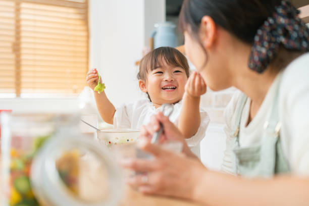 madre y su pequeña hija disfrutando comiendo ensalada y bebiendo batido en casa - asian meal fotografías e imágenes de stock