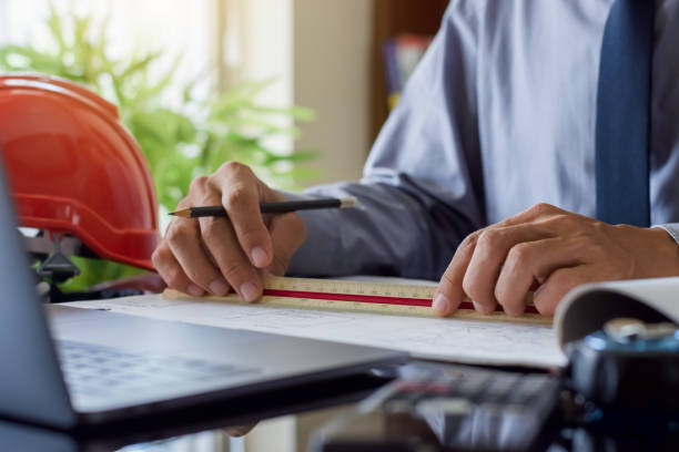 istock Architect man or male engineer work on architectural project with laptop computer and calculator on the desk at office. 1352793616