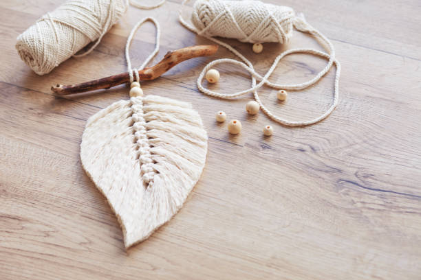 istock Macrame leaf  in natural color and thread windings lying on a wooden table. Cotton rope decor macrame to make your room more cozy and unique. Woman hobby. Handmade wall hanging decor. Copy space 1352807908