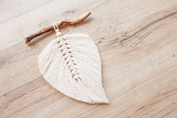 istock Macrame leaf  in natural color and thread windings lying on a wooden table. Cotton rope decor macrame to make your room more cozy and unique. Woman hobby. Handmade wall hanging decor. 1352807913