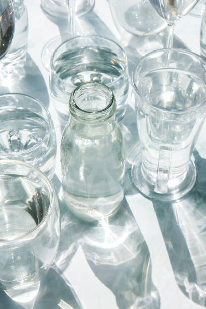 istock Beautiful different glasses stand on white background in sunlight and create shadows. Hard light, long shadows. Creative concept of drinks, alcohol cocktails. Glassware concept 1352811931
