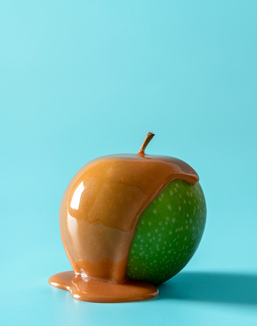 Green apple with caramel sauce isolated a blue background. Delicious caramel apple minimalist on a blue table.