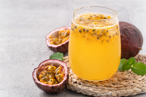 Close up of delicious juicy fresh passion fruit with sparkling juice on gray table background.