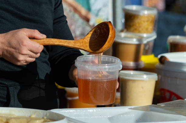 istock a man puts honey in a plastic container with a wooden spoon 1352822168