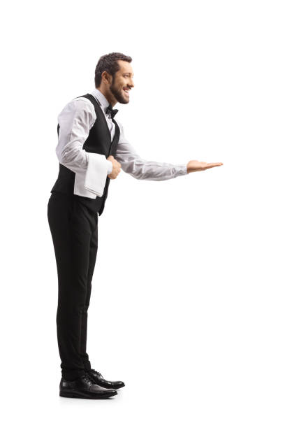 полнометражный профильный снимок вежливого элегантного официанта, жестикулирующего приветствие рукой - greeting welcome sign waiter butler стоковые фото и изображения