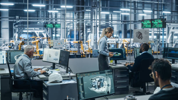 istock Car Factory: Team of Automotive Engineers Working, Using Computers to Design Advanced 3D Models for High-Tech Engines. Automated Robot Arm Industrial Assembly Line Manufacturing Electric Vehicles 1352825017