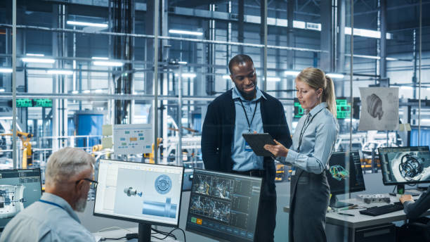 car factory office: female engineer talks with male scientist, use tablet computer to design production conveyor for advanced power engines. automated robot arm assembly line manufacturing vehicles - manufacturing imagens e fotografias de stock