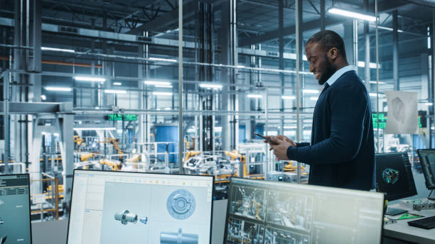istock Car Factory Office: Portrait of Successful Black Male Chief Engineer Using Tablet Computer in Automated Robot Arm Assembly Line Manufacturing High-Tech Electric Vehicles. Side View Shot 1352825130