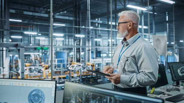 istock Car Factory Office: Portrait of Successful Caucasian Male Chief Engineer Using Tablet Computer in Automated Robot Arm Assembly Line Manufacturing High-Tech Electric Vehicles. Side View Shot 1352825152