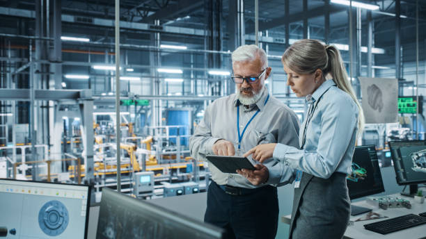 istock Car Factory: Female Project Manager Talks to Male Automotive Engineer, Plan Strategy Using Tablet Computer. Automated Robot Arm Assembly Line Production Conveyor Manufacturing Electric Vehicles 1352825158
