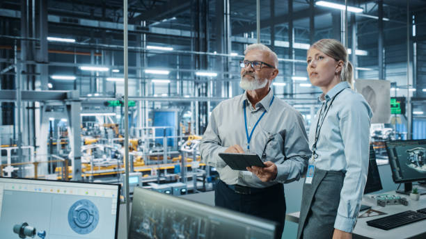 istock Car Factory: Female Project Manager Talks to Male Automotive Engineer, Plan Strategy Using Tablet Computer. Automated Robot Arm Assembly Line Production Conveyor Manufacturing Electric Vehicles 1352825220