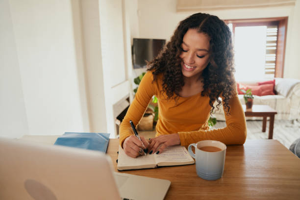 istock Multi-cultural female happily writing in notebook. Young professional remote working with laptop in modern apartment 1352825565
