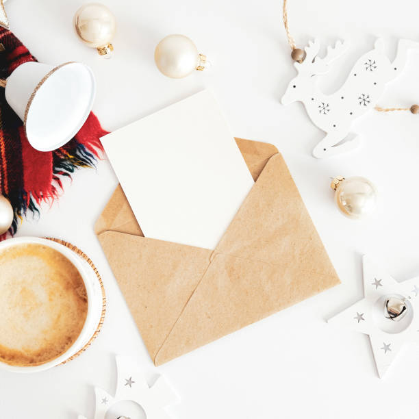 istock Christmas composition. Craft paper envelope with blank paper card mockup, scarf, coffee cup, vintage Christmas decoration on white table. Flat lay, top view, copy space. 1352825682