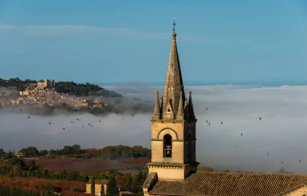 view of church tower at Bonnieux hiitop village in  provence  France with Lacoste in the background misty autumn morning seen from the luberon mountain .