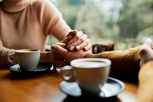 Close up of unrecognizable couple holding hands in a cafe.