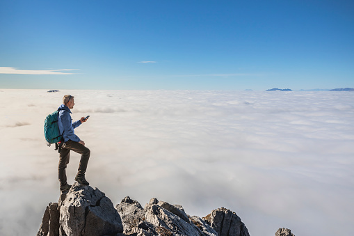 Mature man checking smartphone app on top of the mountain
